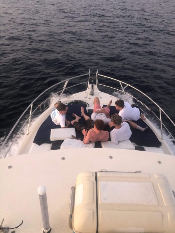 A dynamic action shot capturing two anglers from the 'Blue Marlin' fighting an immense Bluefin Tuna in golden hour off the Marbella coast. The fisherman in blue (gimbal belt) holds a tensed, bent rod while the assistant (full harness) assists. Multiple Penn International and Shimano Tiagra reels are visible. The stunning Sierra Blanca mountains (La Concha peak) are the background during a professional Big Game fishing trip, departing from Marina La Bajadilla.