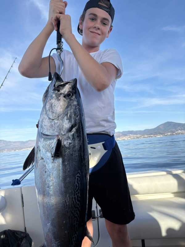 Happy family celebrating a child’s first fish catch using specialized lightweight gear for kids, onboard the Blue Marlin fishing boat in Marina La Bajadilla, Marbella.